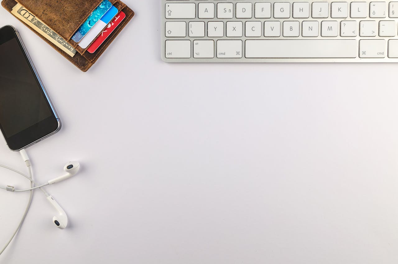 Flat lay of minimalist desk setup featuring a smartphone, keyboard, earphones, and wallet for productivity inspiration.
